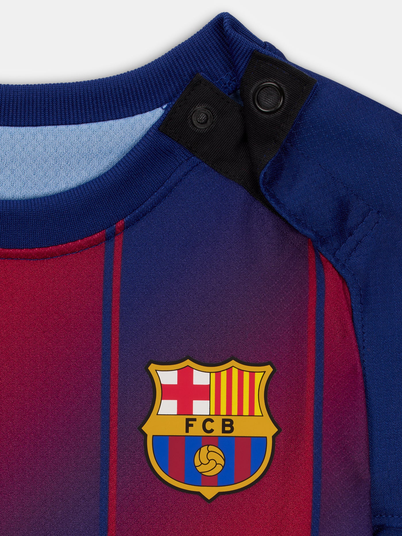 Flat lay of a Baby sized FC Barcelona home kit, including a red and blue striped jersey with Nike and Spotify logos, matching shorts with the Barça crest, and blue socks with red tops and yellow Nike swooshes.

