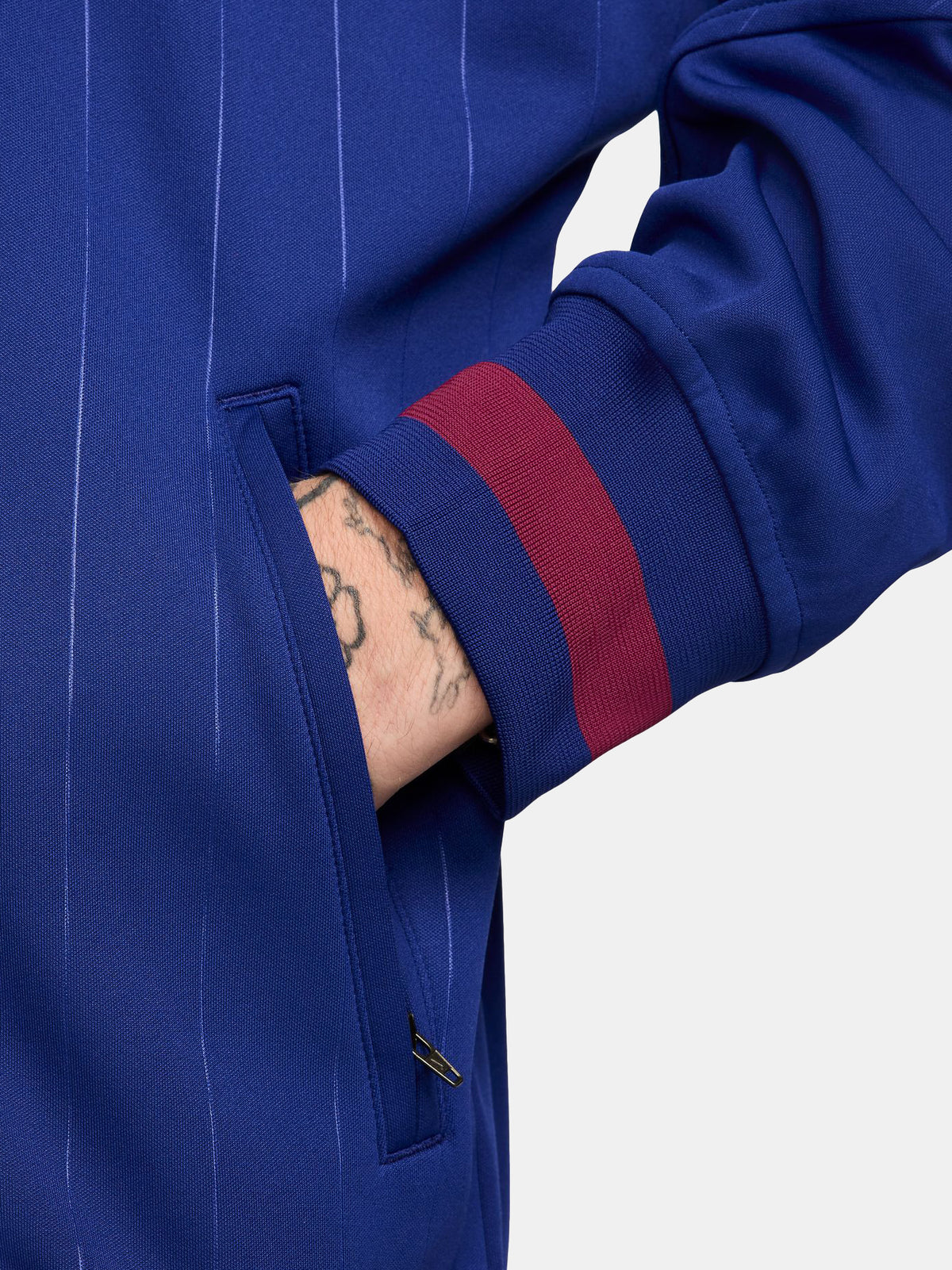 FC Barcelona 2025/26 retro-inspired track jacket featuring a royal blue base with fine vertical pinstripes, yellow Nike swoosh, and the club crest on the chest. Ribbed cuffs and hem include red and navy stripe details for a vintage finish.
