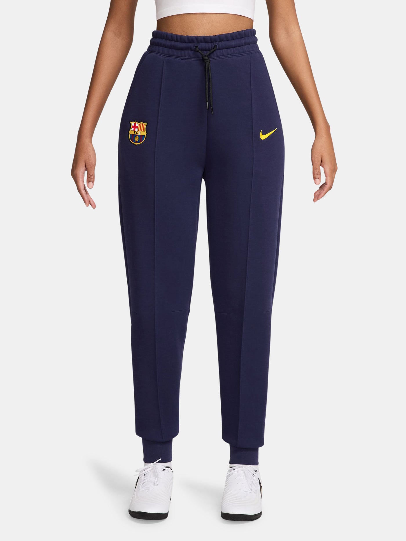 FC Barcelona women’s fleece joggers in navy blue. These pants feature a high-rise fit with an elastic drawstring waistband, ribbed cuffs, and front seams. The Barça crest and yellow Nike swoosh are placed on the front for a bold and sporty finish. Ideal for everyday comfort or casual training wear.
