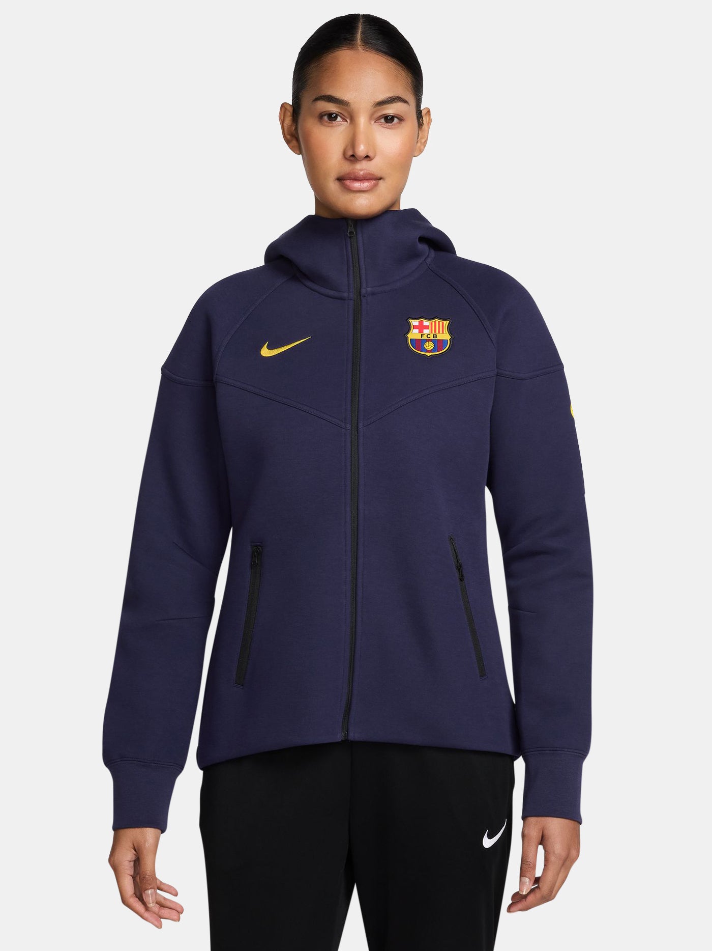 FC Barcelona women’s full-zip hoodie in navy blue. This jacket features a streamlined design with a high collar and front zip, complete with the club crest and yellow Nike swoosh. Designed for comfort and warmth with zippered side pockets and a modern, sporty silhouette.
