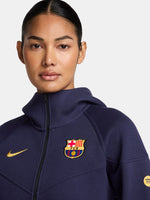 FC Barcelona women’s full-zip hoodie in navy blue. This jacket features a streamlined design with a high collar and front zip, complete with the club crest and yellow Nike swoosh. Designed for comfort and warmth with zippered side pockets and a modern, sporty silhouette.
