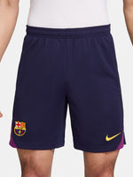 Close-up of a person wearing the FC Barcelona 2025/26 home shorts, featuring a navy blue design with the club crest on the left leg and a yellow Nike logo on the right, shown against a white background.
