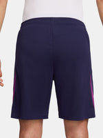 Close-up of a person wearing the FC Barcelona 2025/26 home shorts, featuring a navy blue design with the club crest on the left leg and a yellow Nike logo on the right, shown against a white background.