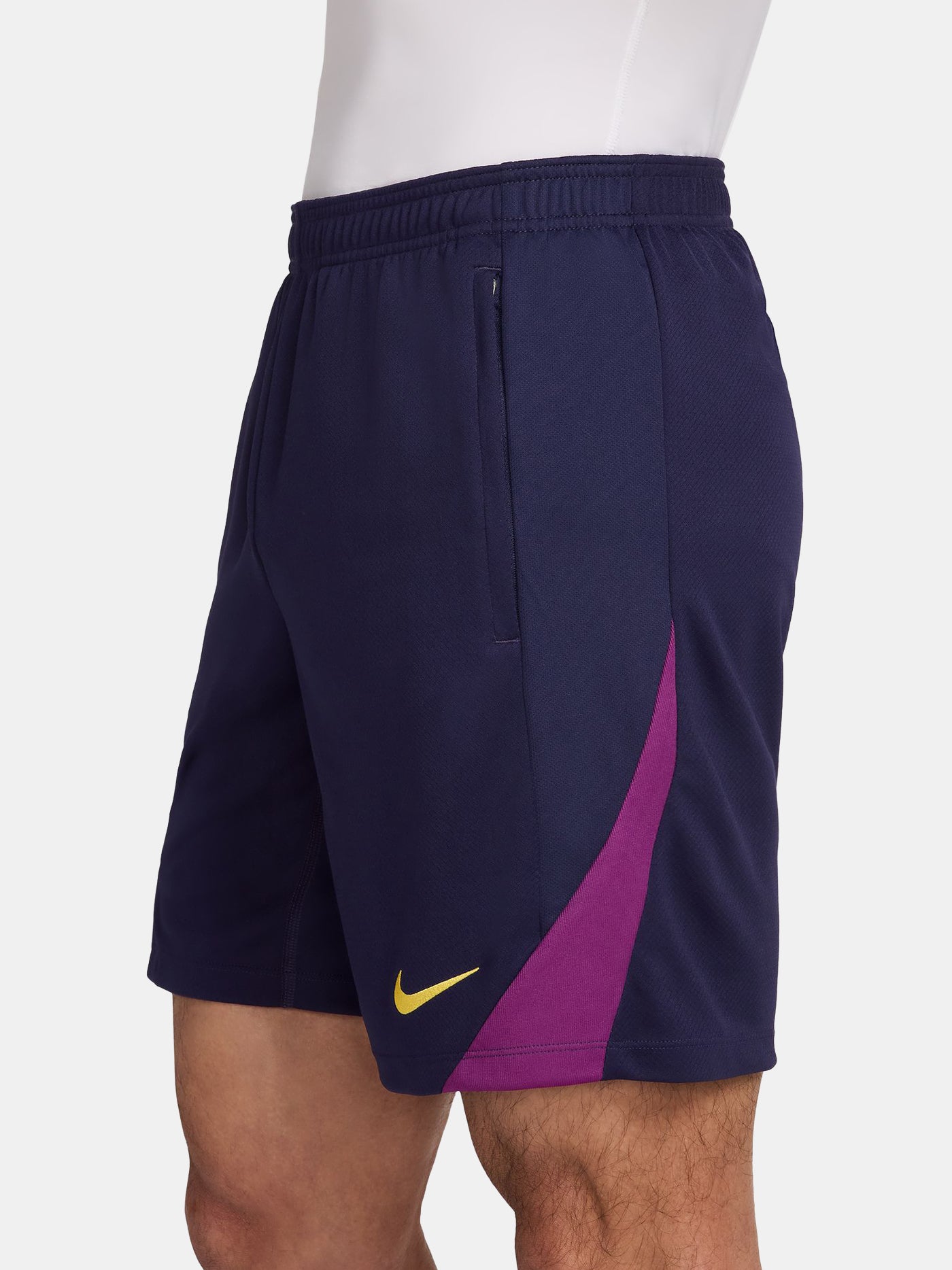 Close-up of a person wearing the FC Barcelona 2025/26 home shorts, featuring a navy blue design with the club crest on the left leg and a yellow Nike logo on the right, shown against a white background.