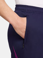 Close-up of a person wearing the FC Barcelona 2025/26 home shorts, featuring a navy blue design with the club crest on the left leg and a yellow Nike logo on the right, shown against a white background.