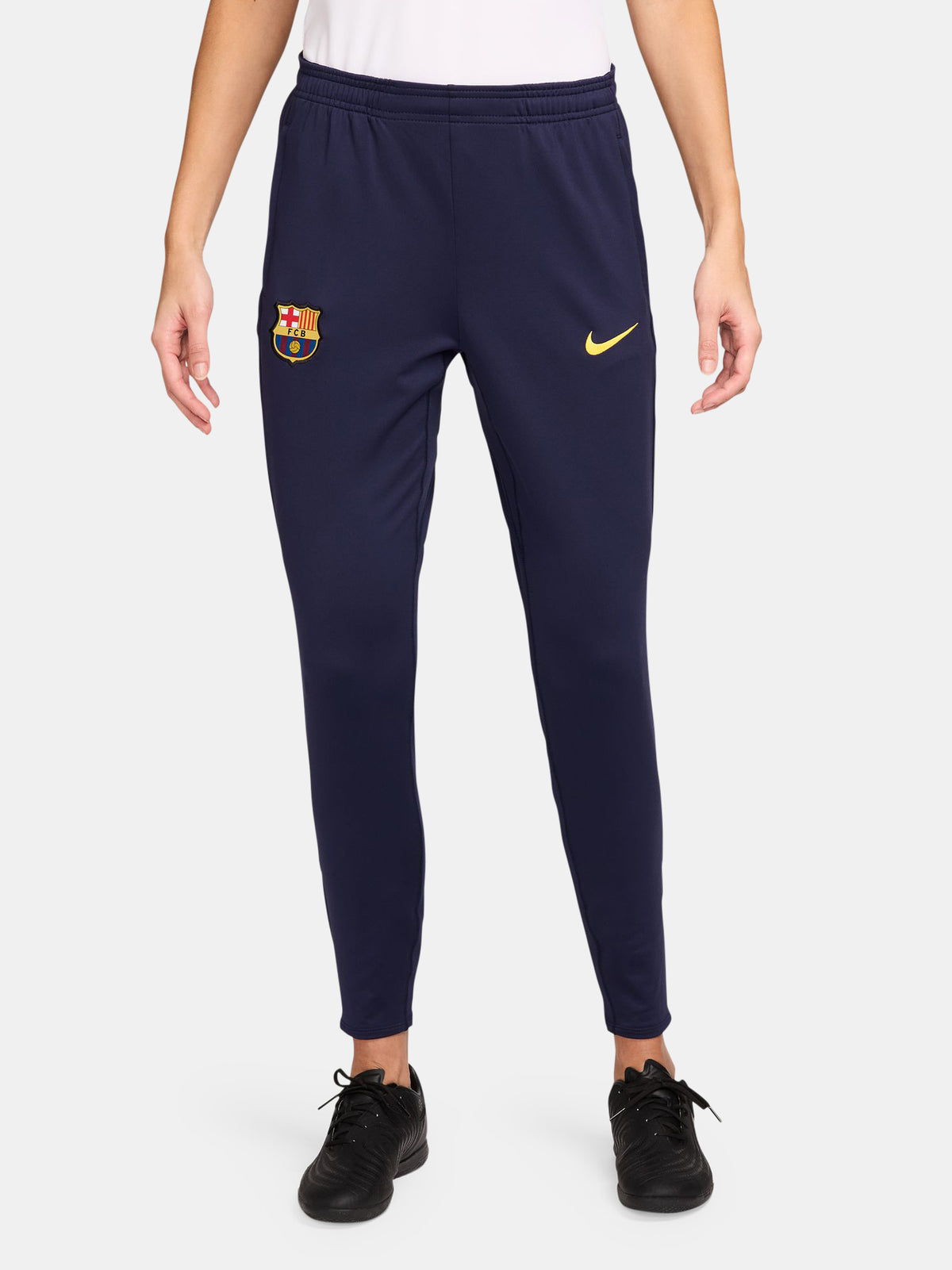 FC Barcelona slim-fit training pants in deep navy blue. These pants feature the official Barça crest on the right leg and a yellow Nike swoosh on the left. Designed with an elastic waistband and tapered legs for a streamlined fit and optimal mobility during training or everyday wear.
