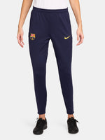 FC Barcelona slim-fit training pants in deep navy blue. These pants feature the official Barça crest on the right leg and a yellow Nike swoosh on the left. Designed with an elastic waistband and tapered legs for a streamlined fit and optimal mobility during training or everyday wear.
