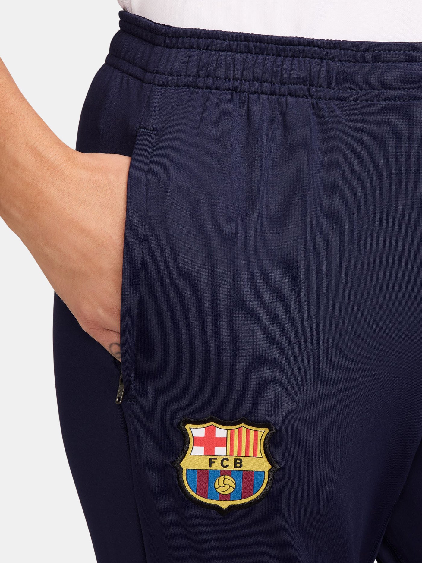 FC Barcelona slim-fit training pants in deep navy blue. These pants feature the official Barça crest on the right leg and a yellow Nike swoosh on the left. Designed with an elastic waistband and tapered legs for a streamlined fit and optimal mobility during training or everyday wear.
