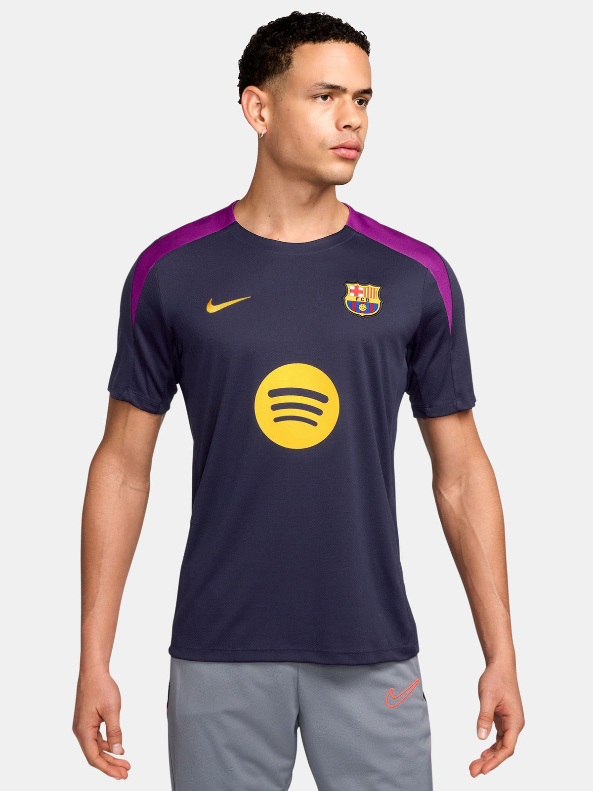FC Barcelona navy training shirt with purple shoulder accents, yellow Nike logo, club crest, and Spotify sponsor, paired with gray shorts featuring a coral Nike logo.