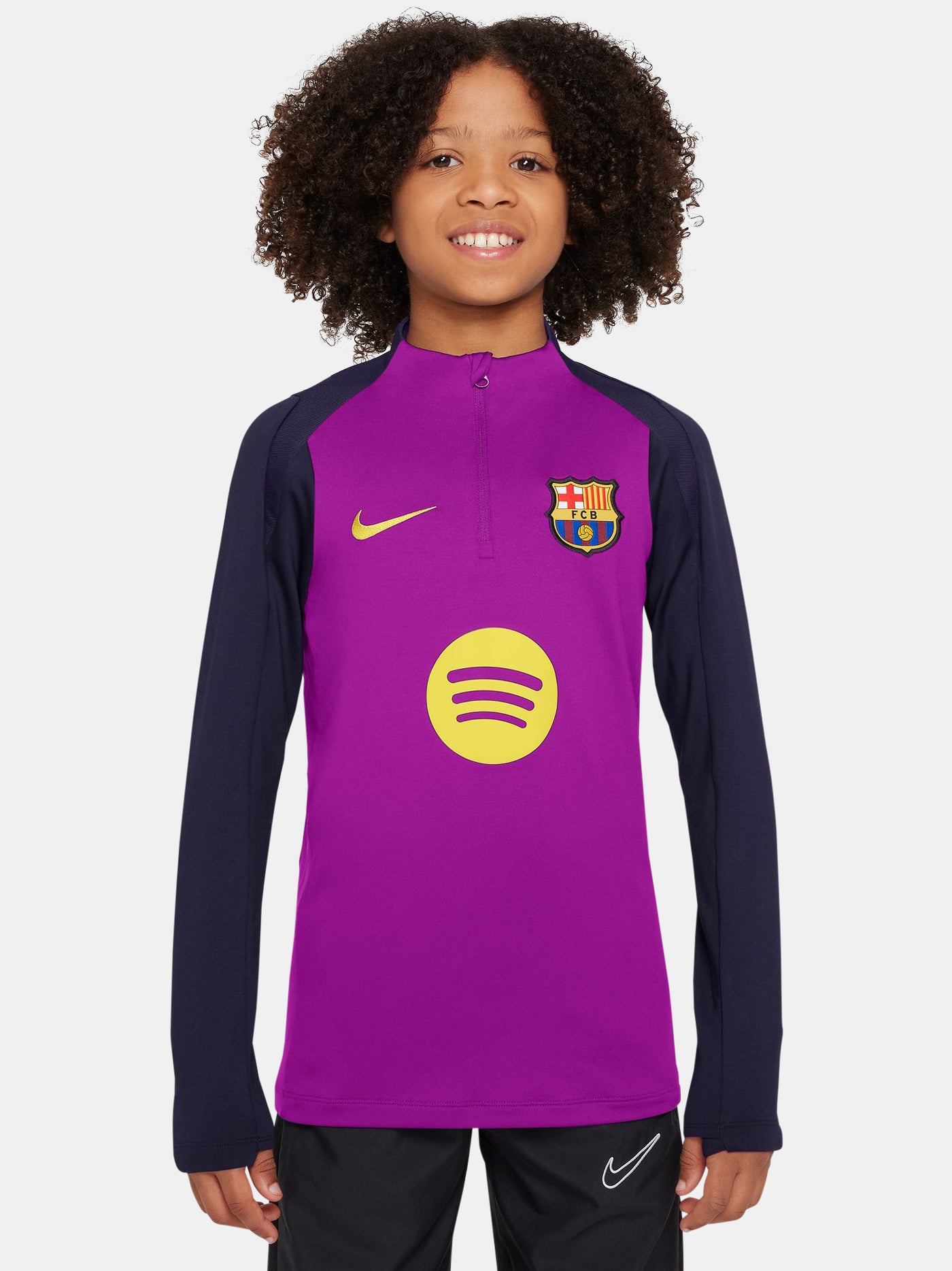 FC Barcelona long-sleeve training top for kids in a vibrant purple body with navy blue sleeves. The top features a yellow Nike swoosh, the Spotify sponsor logo in yellow, and the official Barça crest on the chest. Designed with a half-zip neckline for adjustable ventilation and performance-ready comfort.
