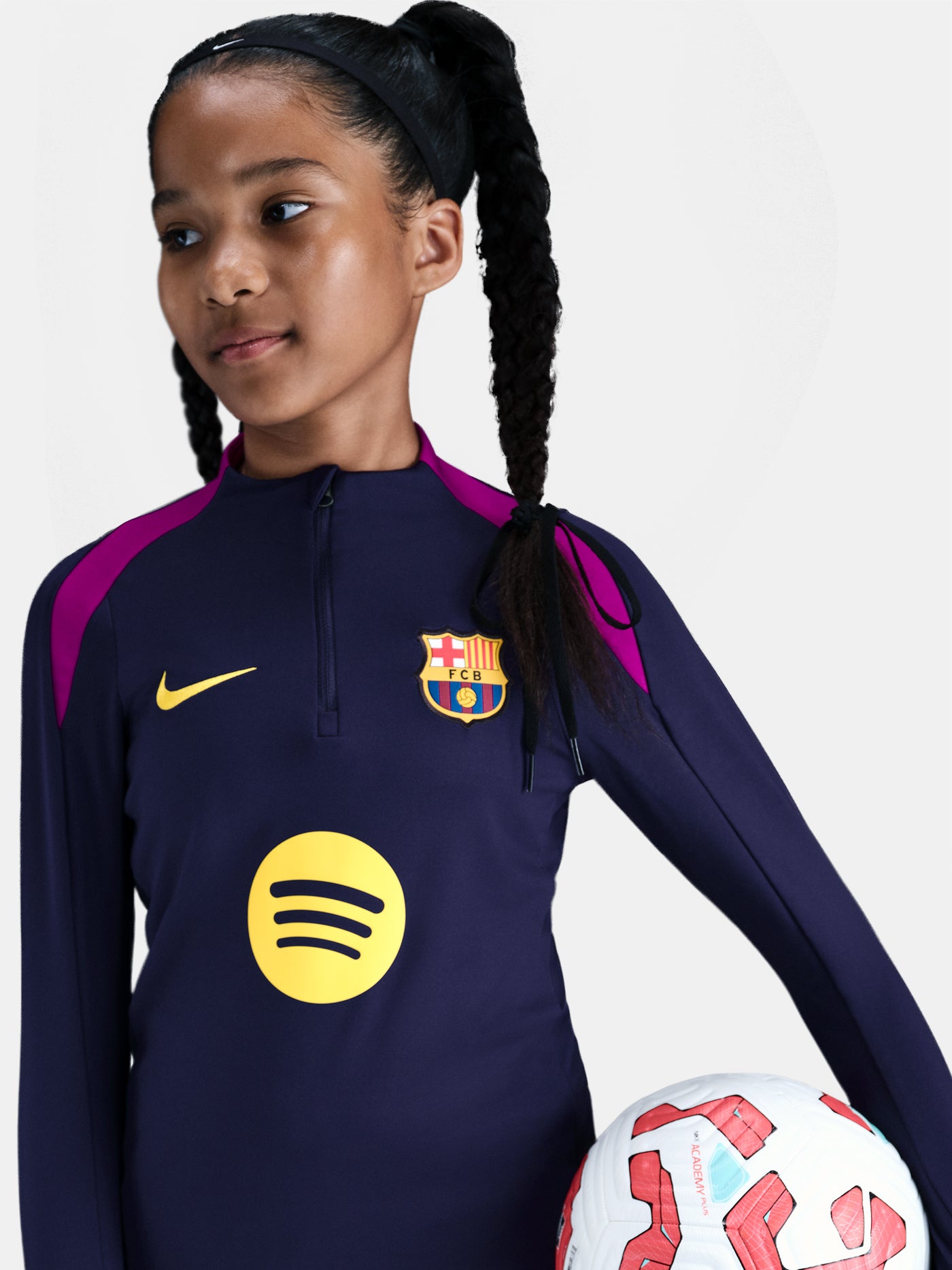 FC Barcelona long-sleeve training top for kids, in deep navy with vibrant magenta shoulder accents. Features include a half-zip design, yellow Nike swoosh, the Spotify sponsor logo, and the club crest prominently displayed—designed for comfort and performance on the pitch.
