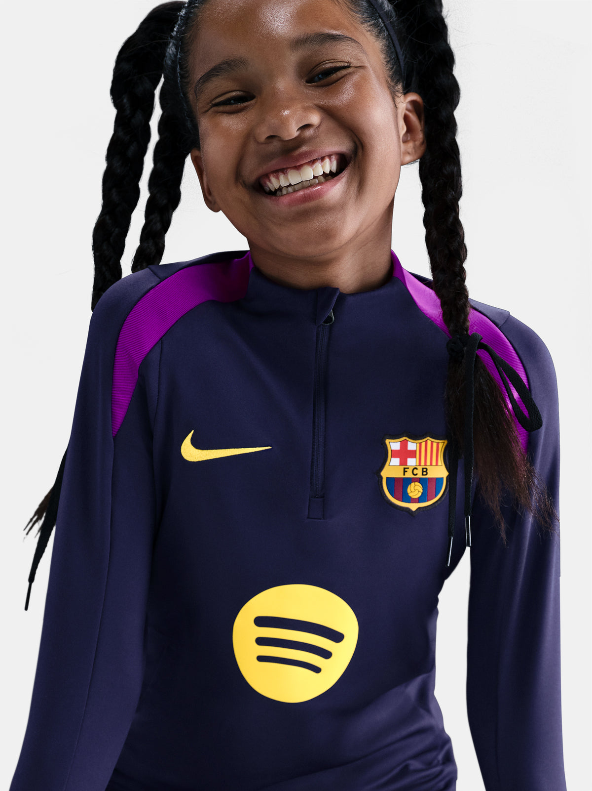 FC Barcelona long-sleeve training top for kids, in deep navy with vibrant magenta shoulder accents. Features include a half-zip design, yellow Nike swoosh, the Spotify sponsor logo, and the club crest prominently displayed—designed for comfort and performance on the pitch.
