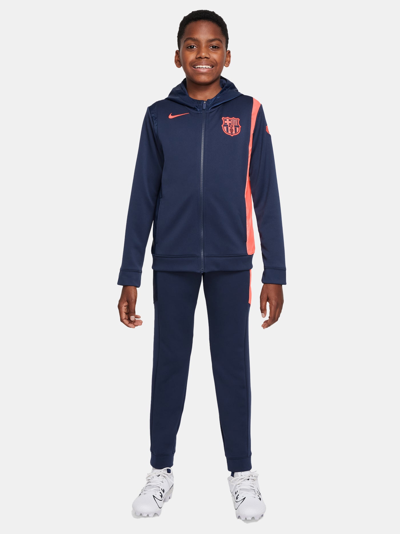 Kid wearing a navy blue FC Barcelona Nike tracksuit with coral details, featuring the club crest and Nike swoosh on the jacket.