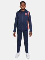 Kid wearing a navy blue FC Barcelona Nike tracksuit with coral details, featuring the club crest and Nike swoosh on the jacket.