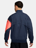 FC Barcelona navy blue jacket with coral details, including a coral sleeve, zipper, Nike logo, and club crest, paired with white Nike pants.