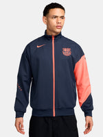 FC Barcelona navy blue jacket with coral details, including a coral sleeve, zipper, Nike logo, and club crest, paired with white Nike pants.