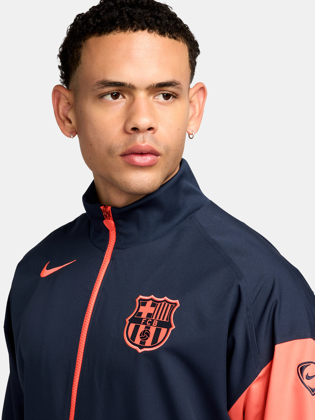 FC Barcelona navy blue jacket with coral details, including a coral sleeve, zipper, Nike logo, and club crest, paired with white Nike pants.
