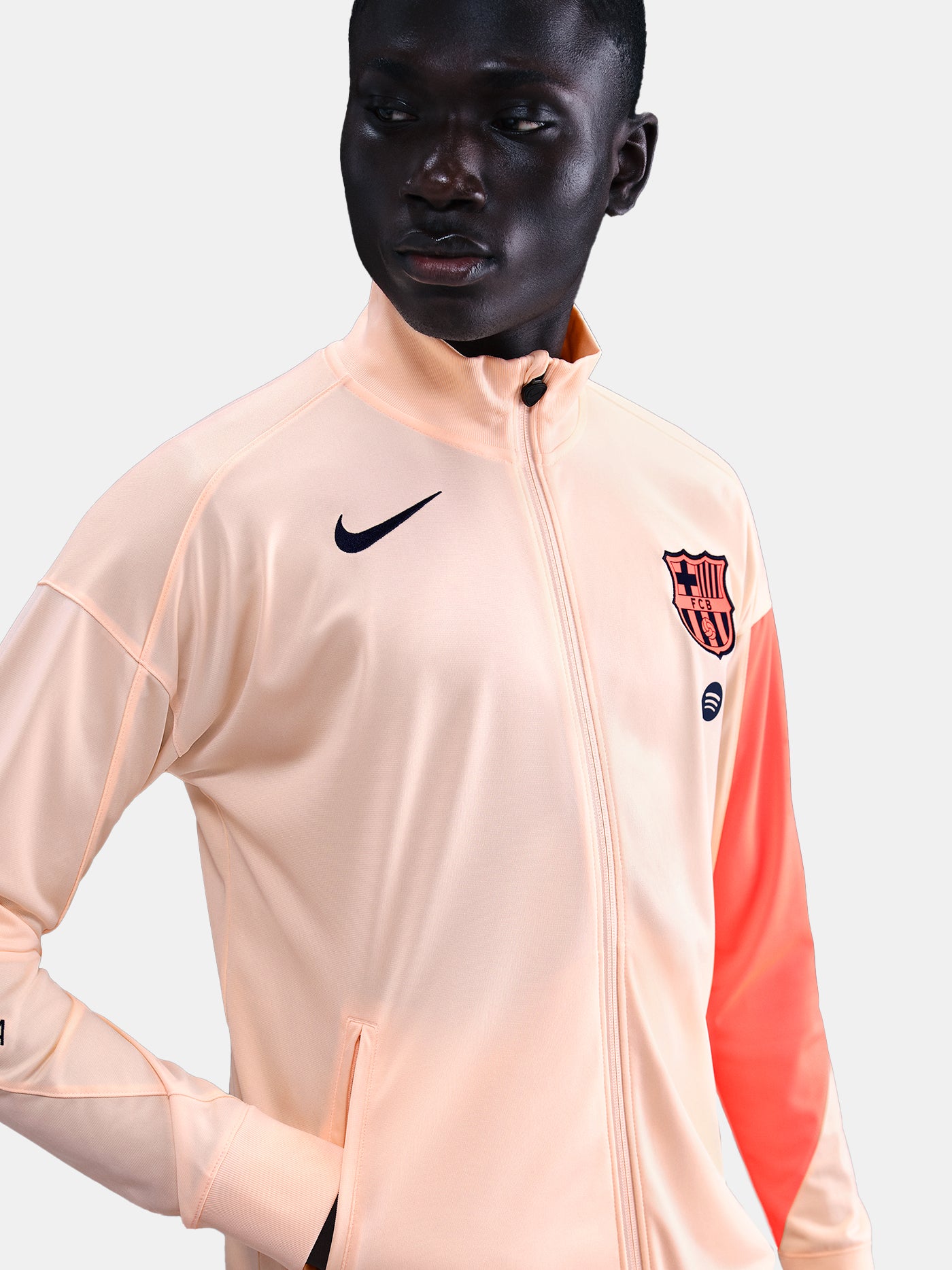 FC Barcelona Nike jacket with coral sleeve detail, paired with navy jogger pants featuring the club crest and Nike swoosh