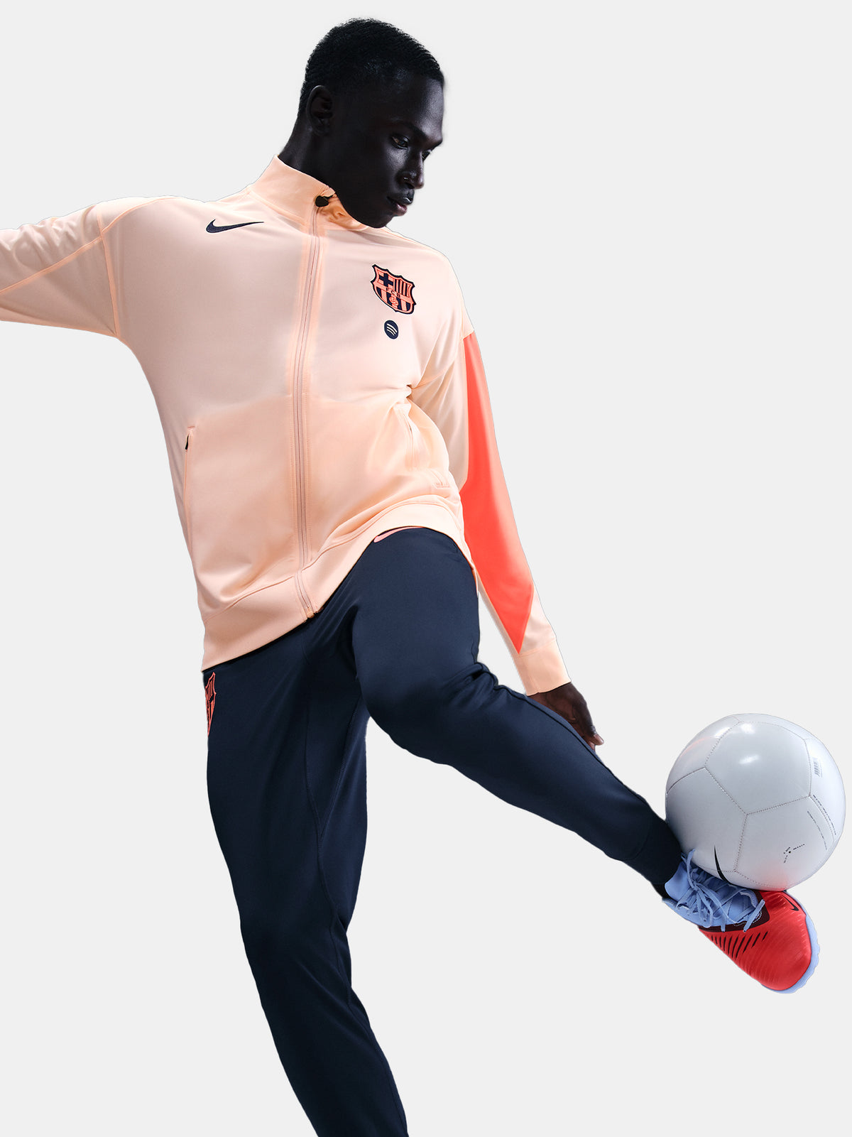 FC Barcelona Nike jacket with coral sleeve detail, paired with navy jogger pants featuring the club crest and Nike swoosh
