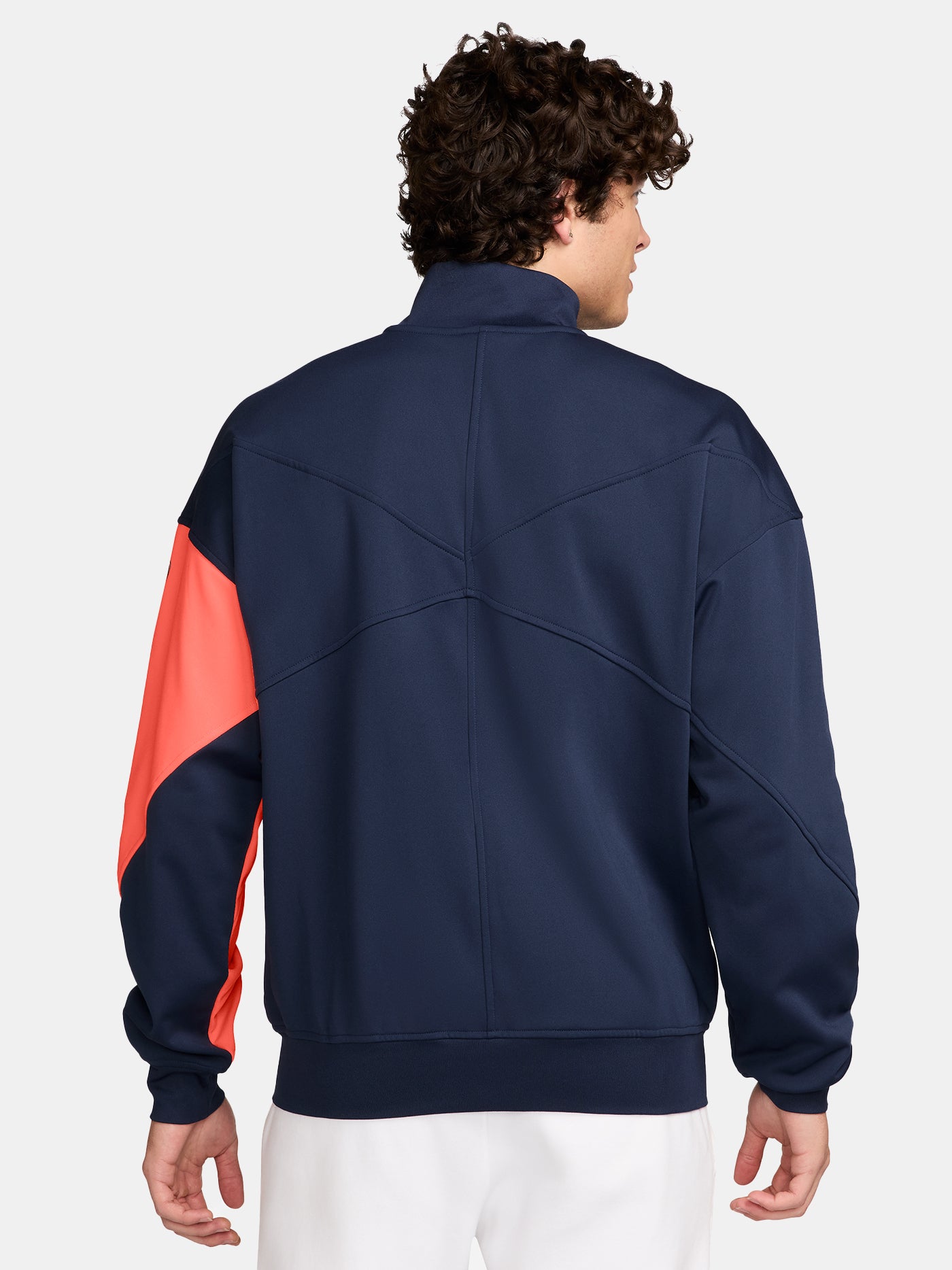 FC Barcelona navy blue jacket with coral details, including a coral sleeve, zipper, Nike logo, and club crest, paired with white Nike pants.