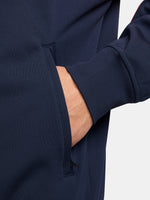 FC Barcelona navy blue jacket with coral details, including a coral sleeve, zipper, Nike logo, and club crest, paired with white Nike pants.