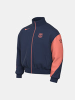 FC Barcelona navy blue jacket with coral details, including a coral sleeve, zipper, Nike logo, and club crest, paired with white Nike pants.