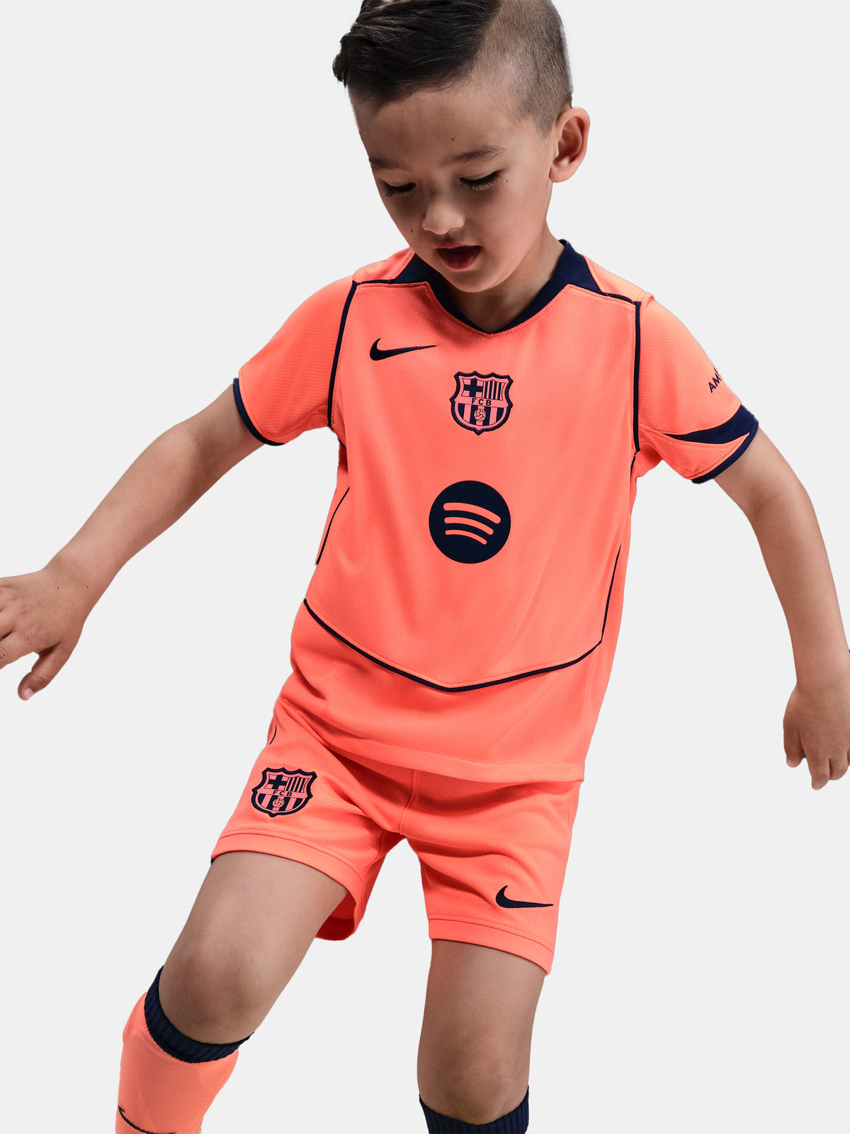FC Barcelona 2025/26 third kit for kids in orange with navy blue details, including shirt, shorts, and socks.