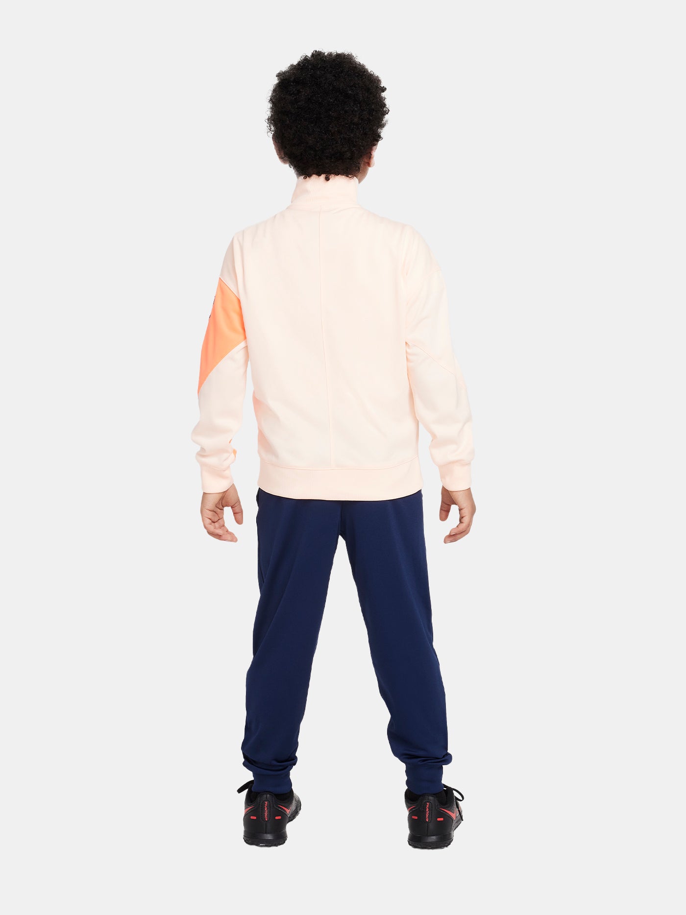 Child wearing a peach and orange FC Barcelona Nike jacket with navy blue pants, both featuring the club crest and Nike swoosh