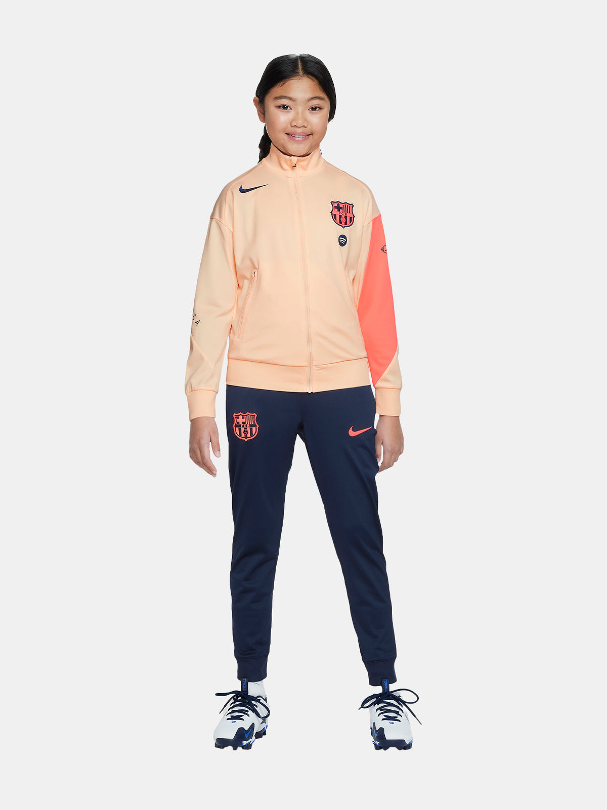 FC Barcelona Nike jacket with coral sleeve detail, paired with navy jogger pants featuring the club crest and Nike swoosh