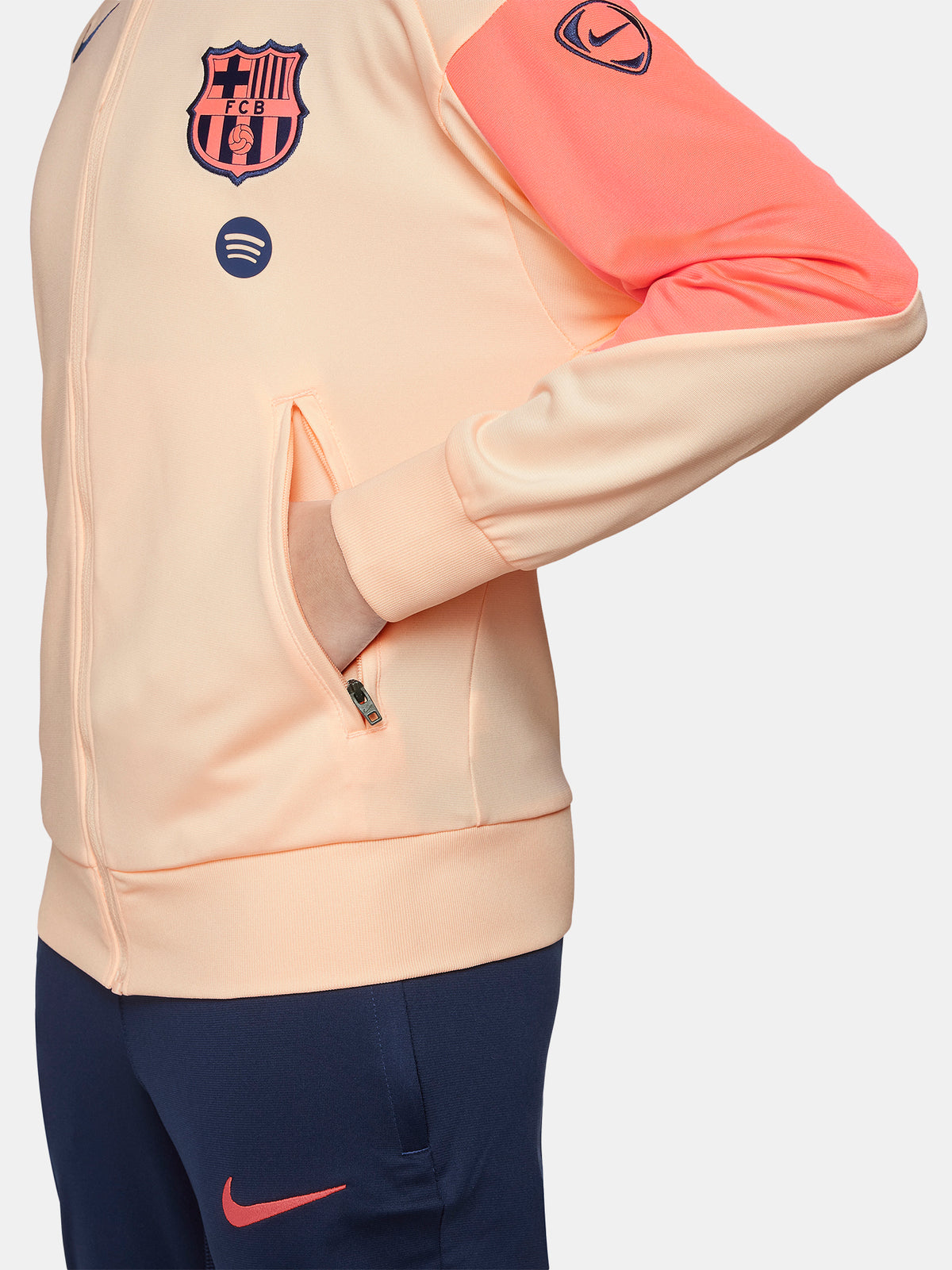 FC Barcelona Nike jacket with coral sleeve detail, paired with navy jogger pants featuring the club crest and Nike swoosh