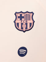 Child wearing a peach and orange FC Barcelona Nike jacket with navy blue pants, both featuring the club crest and Nike swoosh