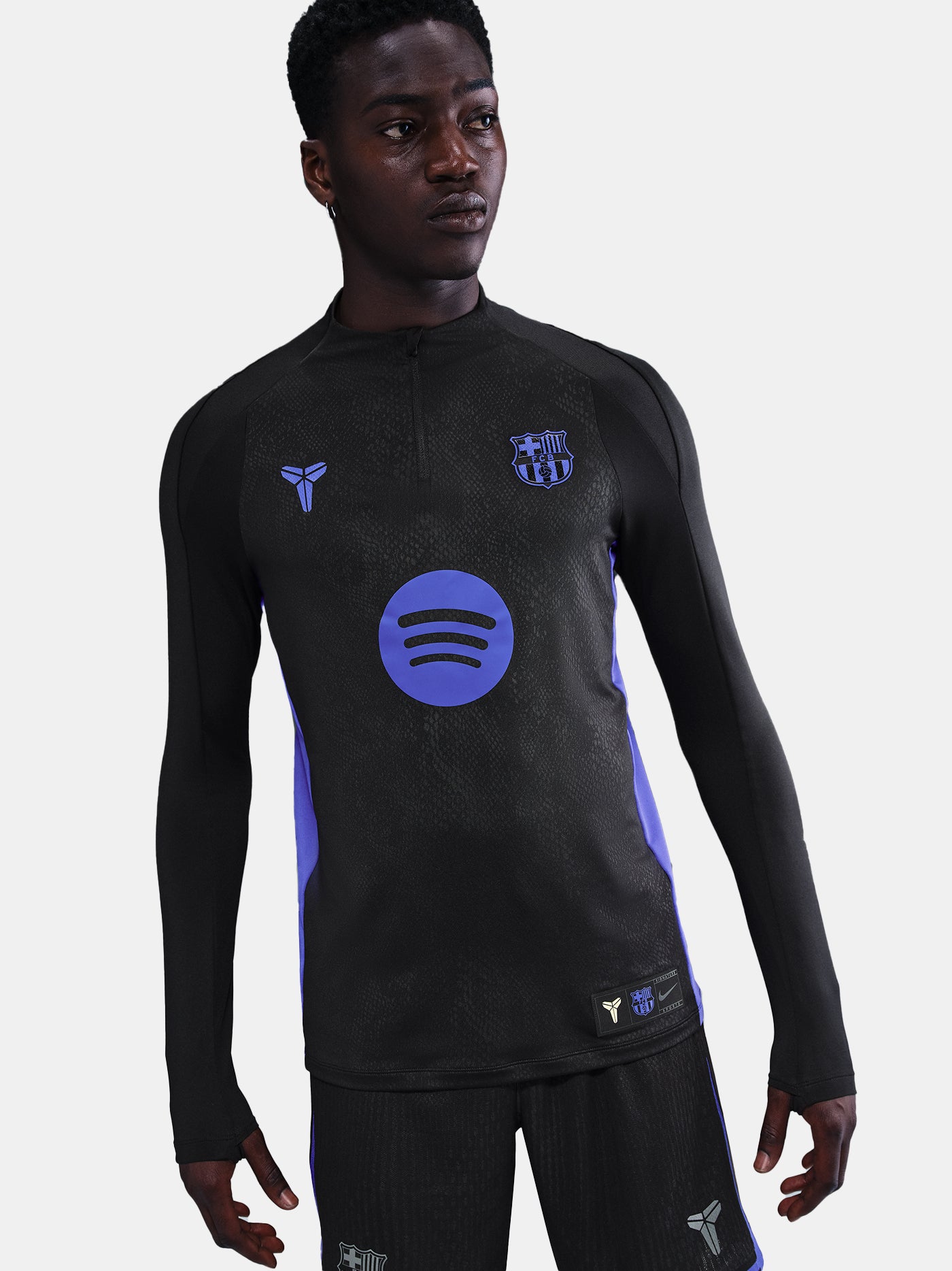 Black FC Barcelona training top with purple details, including the club crest, Nike logo, and Spotify sponsor logo, worn by a person.