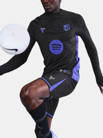 Black FC Barcelona training top with purple details, including the club crest, Nike logo, and Spotify sponsor logo, worn by a person.