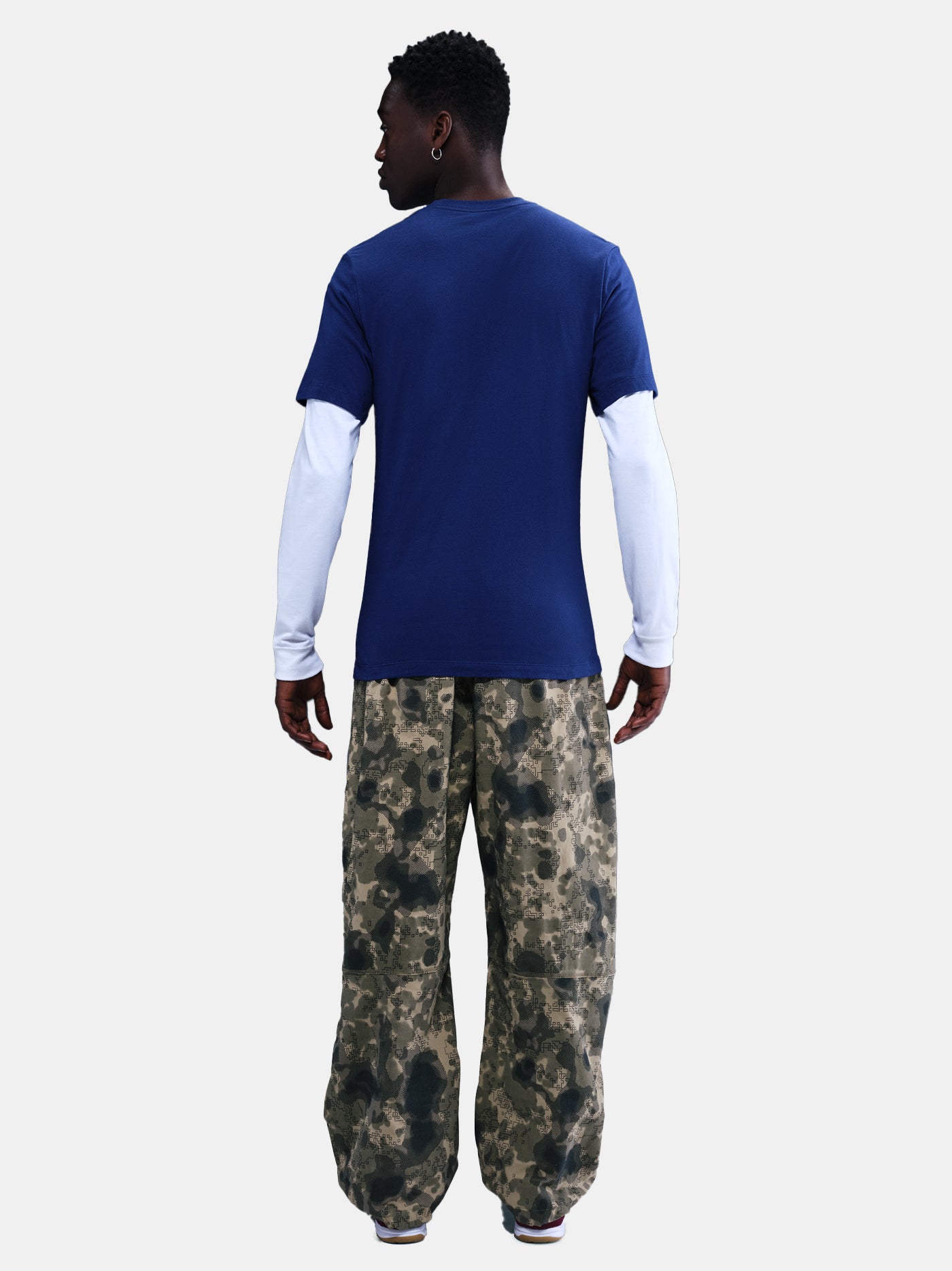 Blue Barça tee with yellow Nike logo, layered over white long sleeves and camo pants. Urban sporty style.
