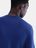 Blue Barça tee with yellow Nike logo, layered over white long sleeves and camo pants. Urban sporty style.
