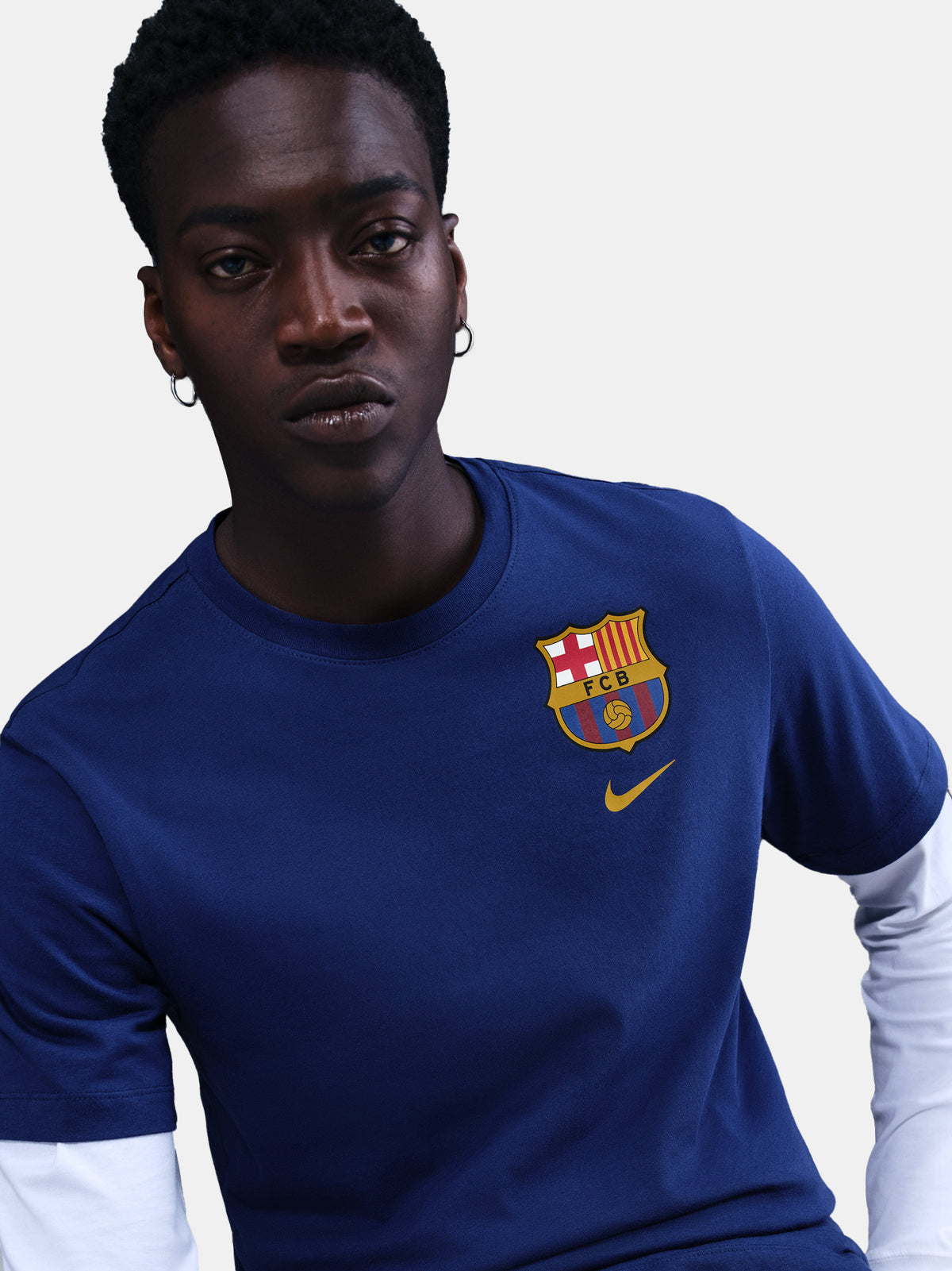 Blue Barça tee with yellow Nike logo, layered over white long sleeves and camo pants. Urban sporty style.
