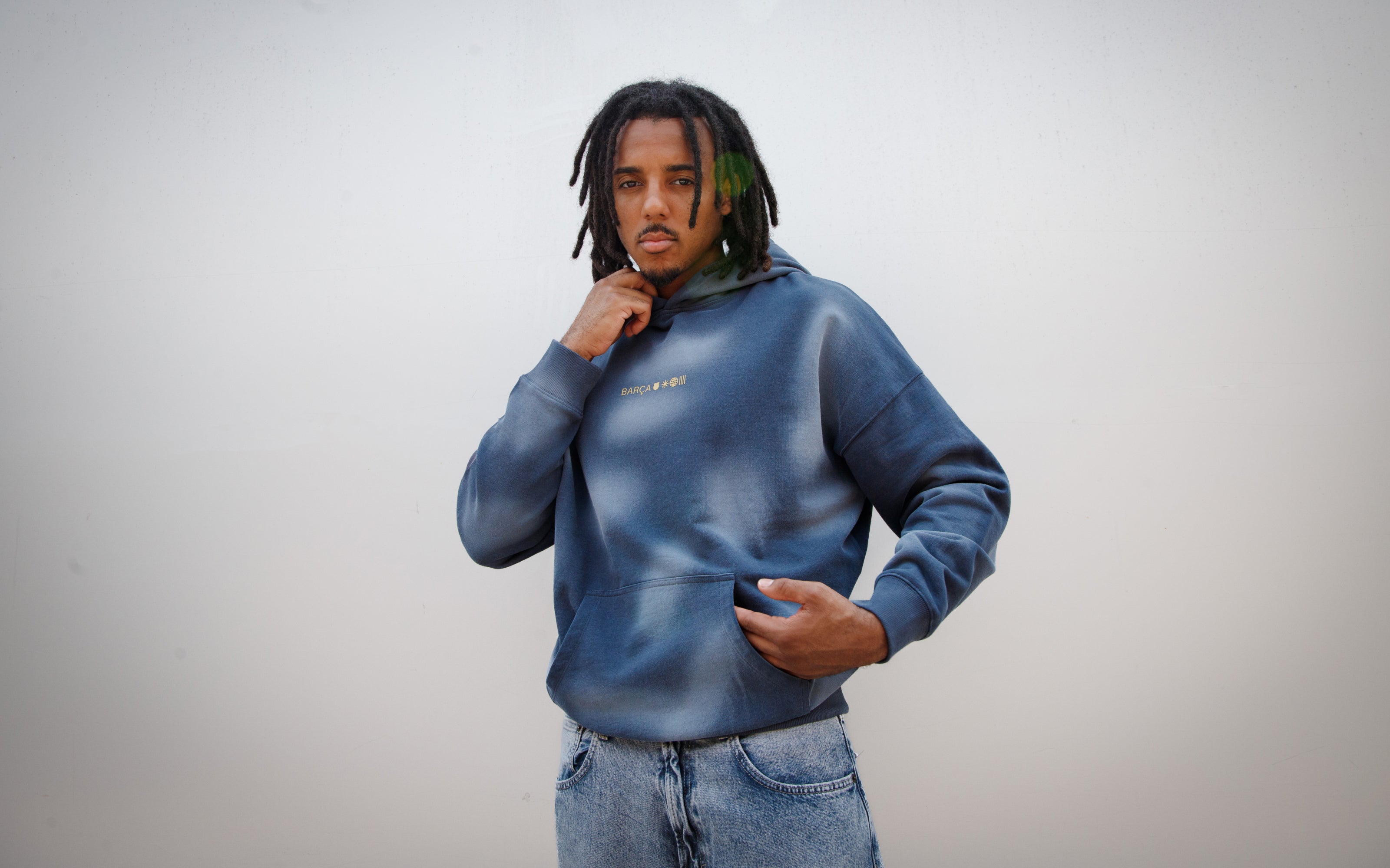 Jules Kounde wearing a faded blue FC Barcelona hoodie with kangaroo pocket and golden 'Barça' text design, paired with light denim jeans