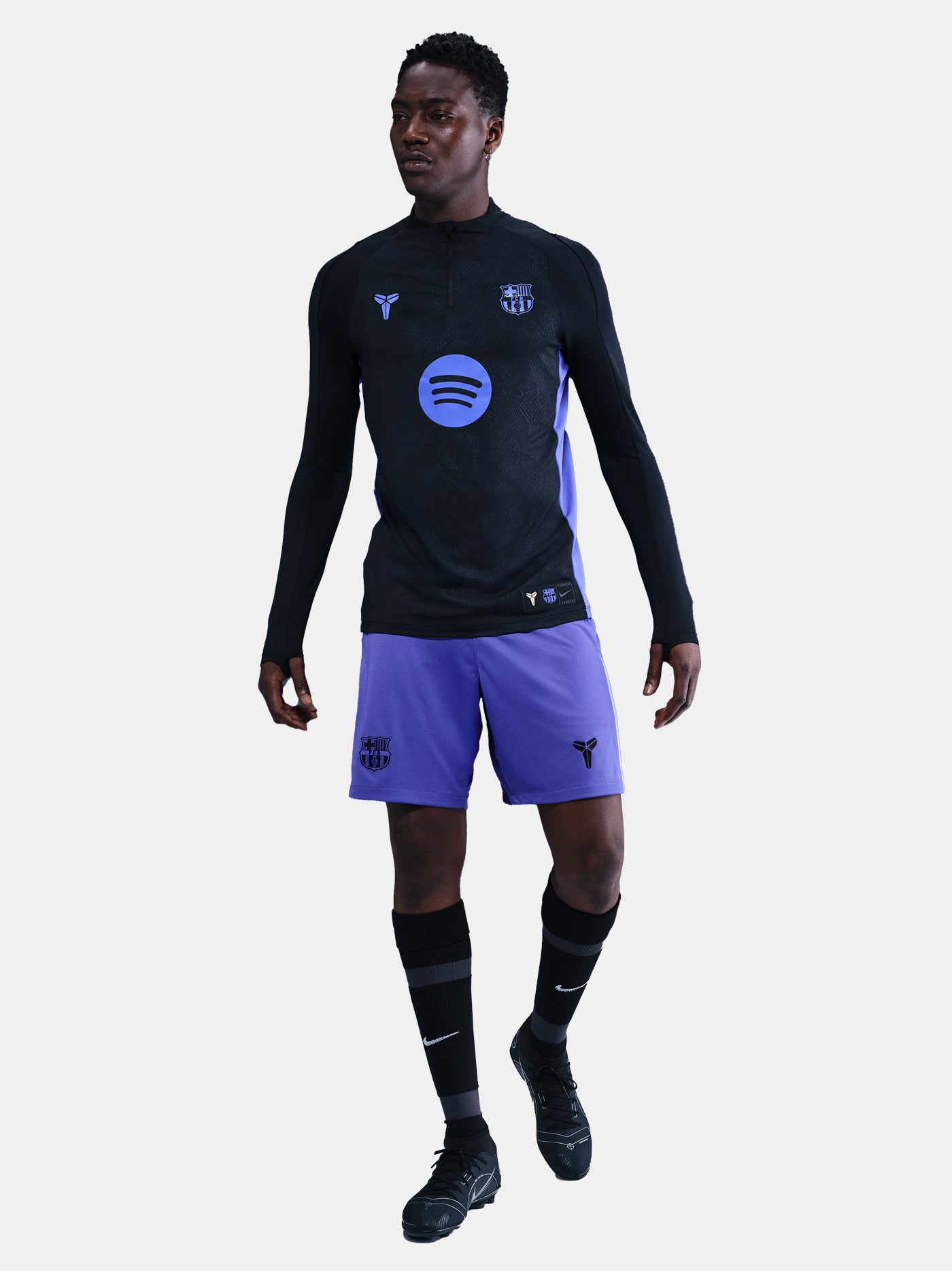 Person wearing a black long-sleeve top and purple shorts with a logo on a white background