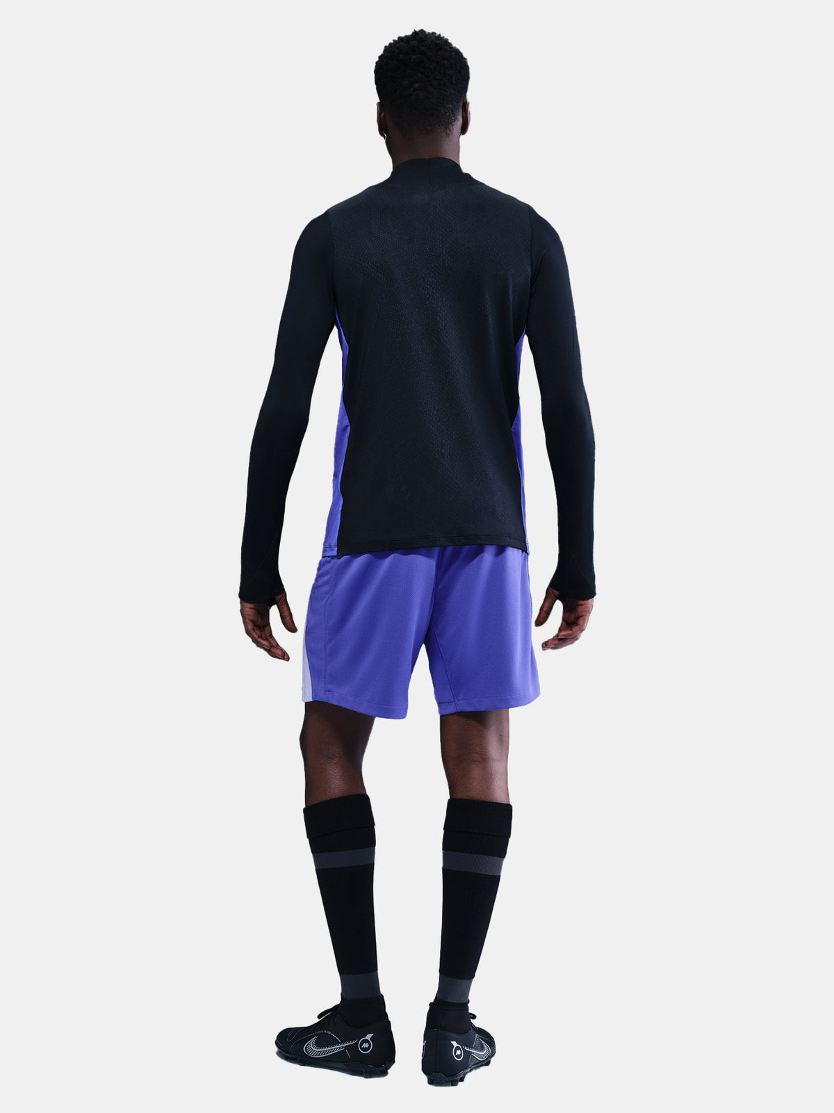 Person wearing a black long-sleeve top and purple shorts on a white background