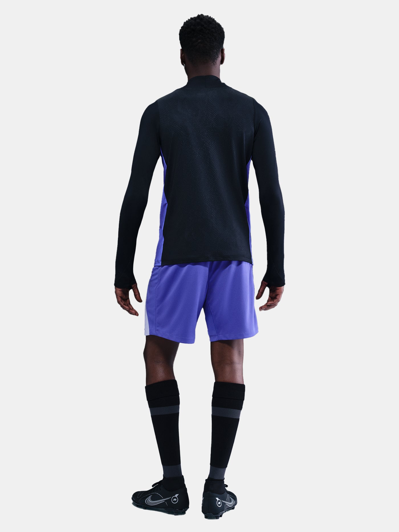 Person wearing a black long-sleeve top and purple shorts on a white background