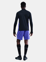 Person wearing a black long-sleeve top and purple shorts on a white background