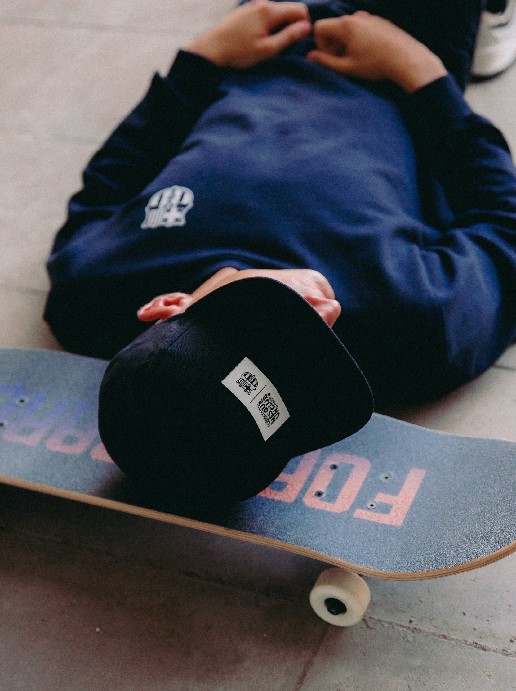 Black flat-brim cap featuring a rectangular white patch on the front with the FC Barcelona crest and the slogan "Més que un club" printed in black.