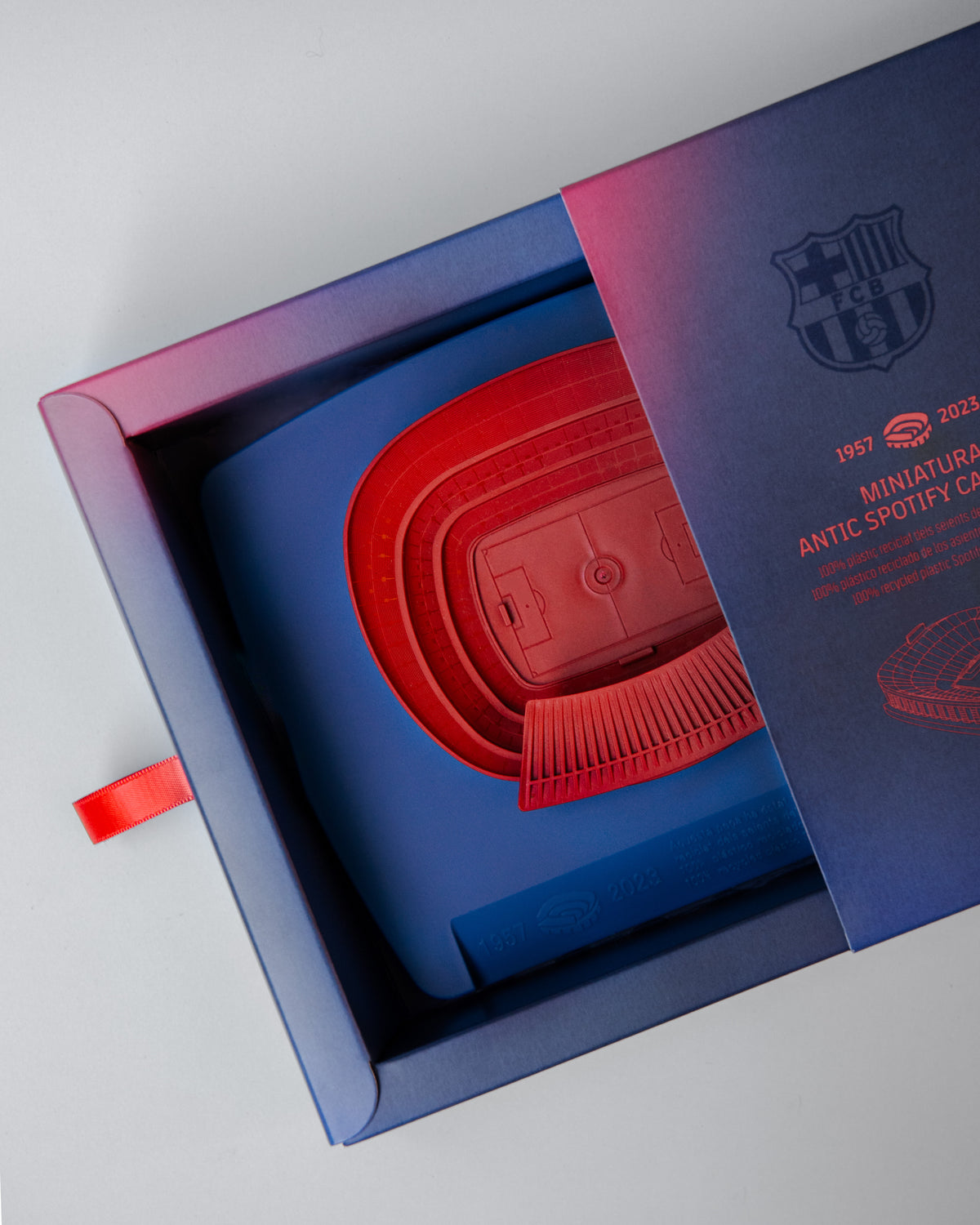 Red 3D miniature model of FC Barcelona’s Camp Nou stadium, placed on a blue surface. The model features detailed tiers, seating sections, and architectural elements of the iconic venue