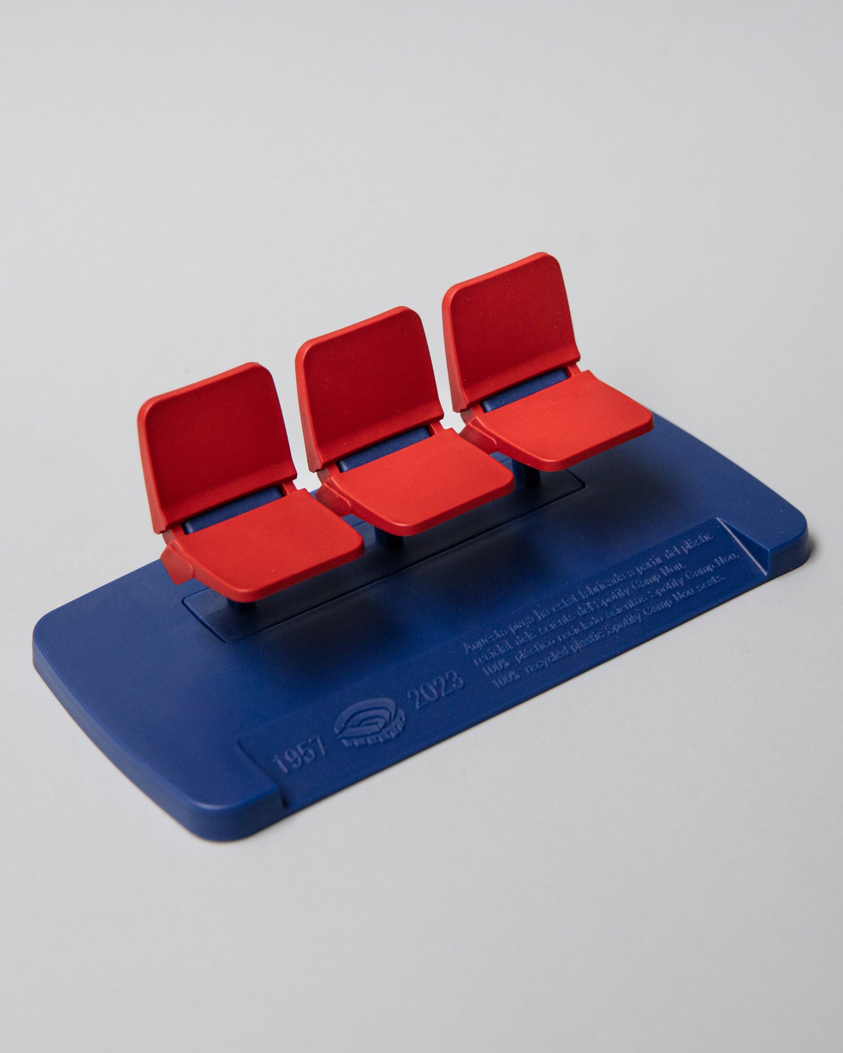 Miniature display of three iconic red Camp Nou stadium seats mounted on a blue base, commemorating the years 1957–2023, marking the historical timeline of FC Barcelona’s legendary stadium.