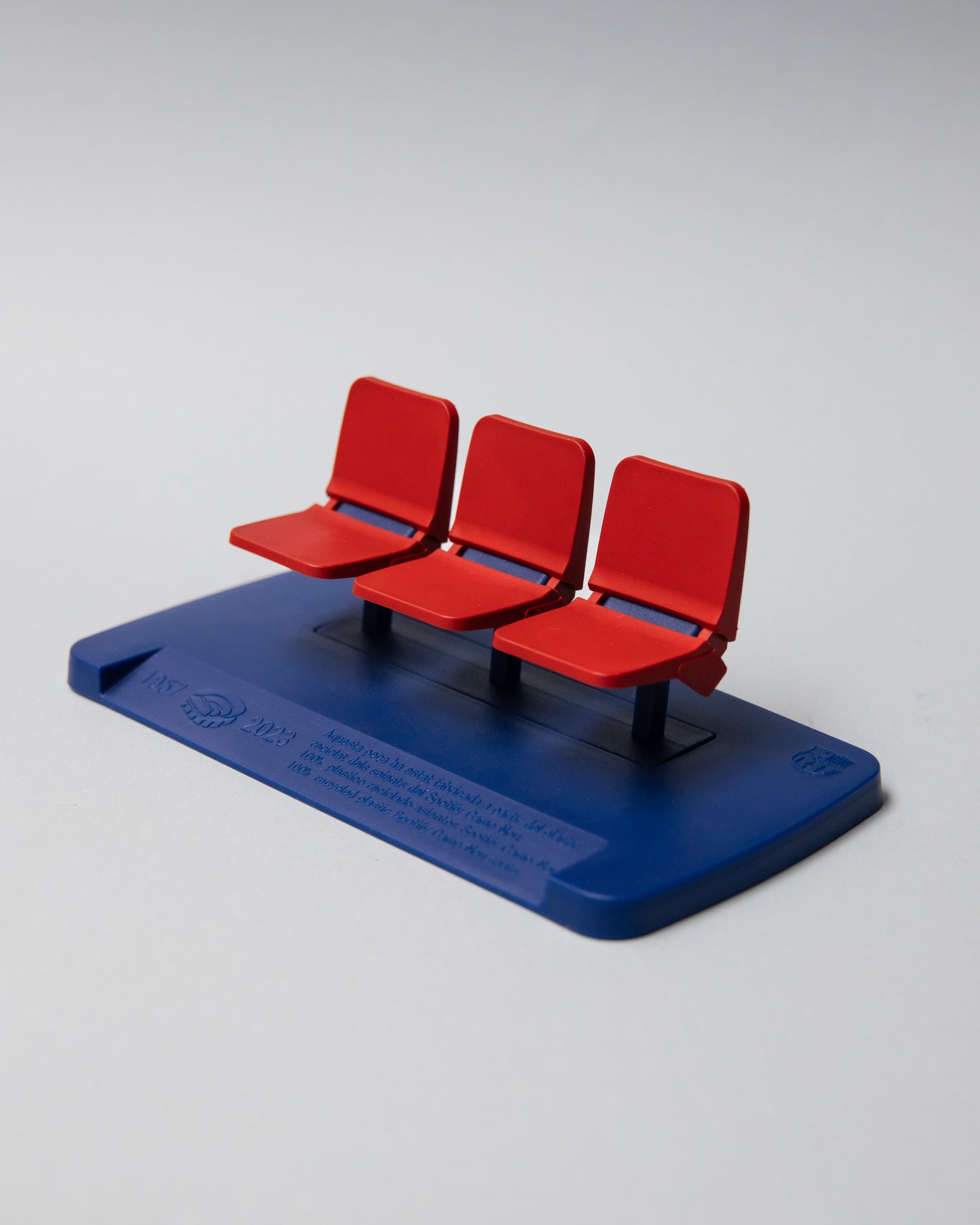 Miniature display of three iconic red Camp Nou stadium seats mounted on a blue base, commemorating the years 1957–2023, marking the historical timeline of FC Barcelona’s legendary stadium.