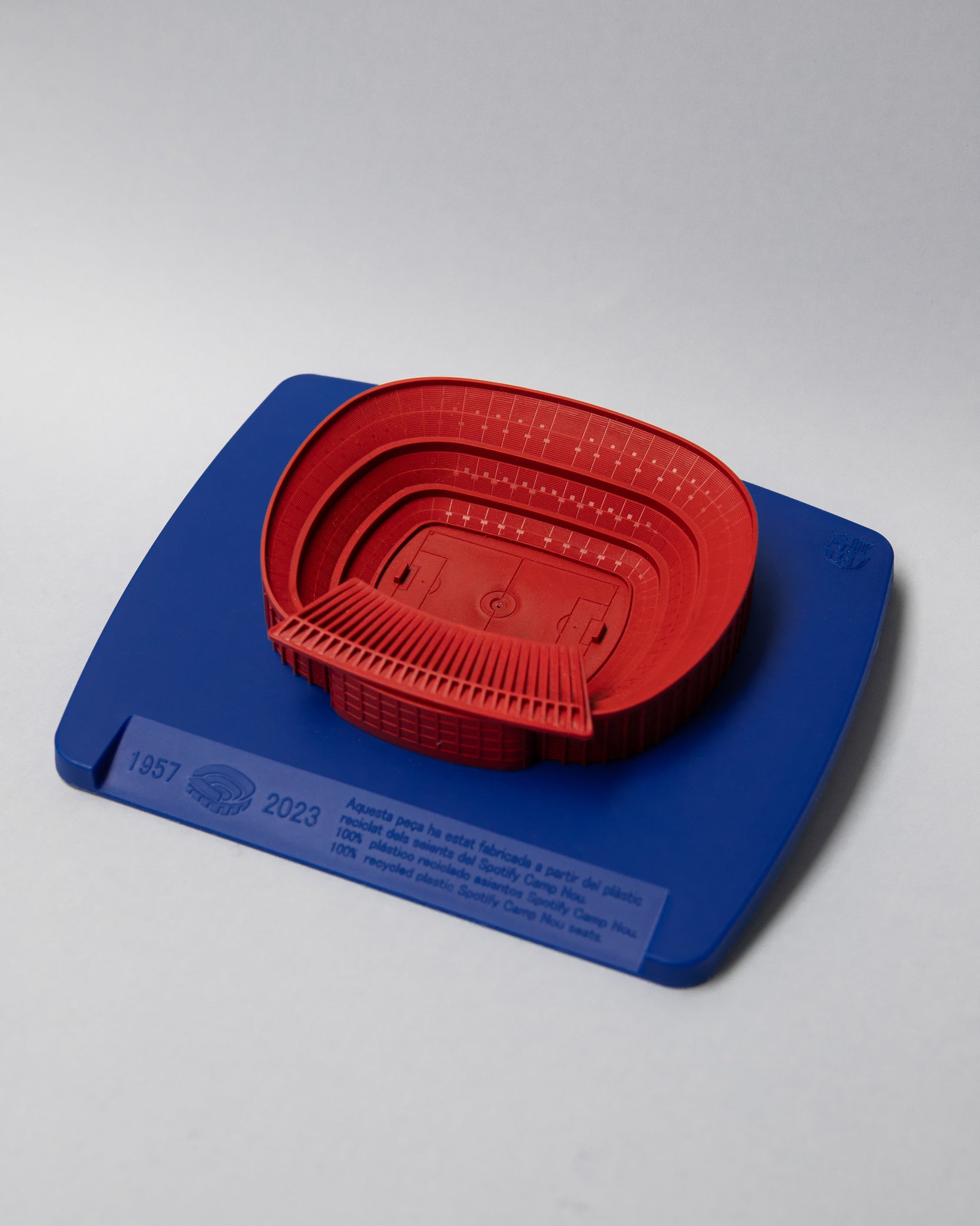 Red 3D miniature model of FC Barcelona’s Camp Nou stadium, placed on a blue surface. The model features detailed tiers, seating sections, and architectural elements of the iconic venue