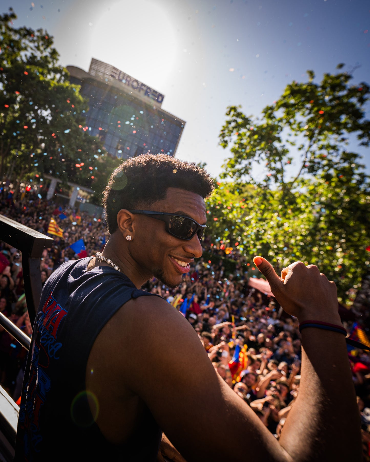 Man in sunglasses giving a thumbs up in front of a crowd with confetti
