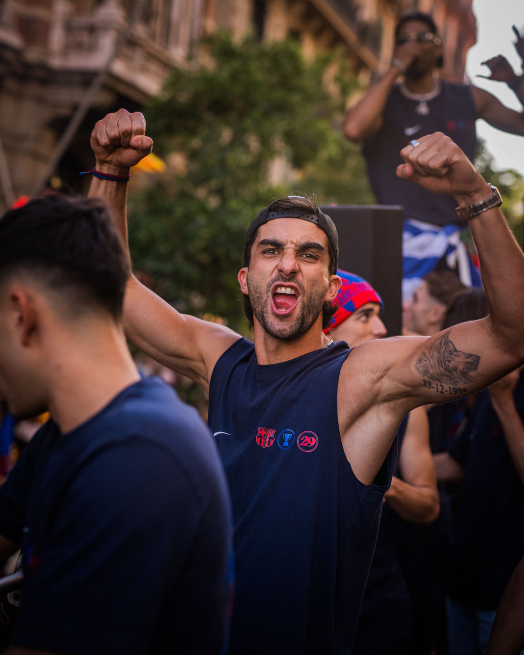 Man in a dark blue tank top with a logo, arms raised in a crowd