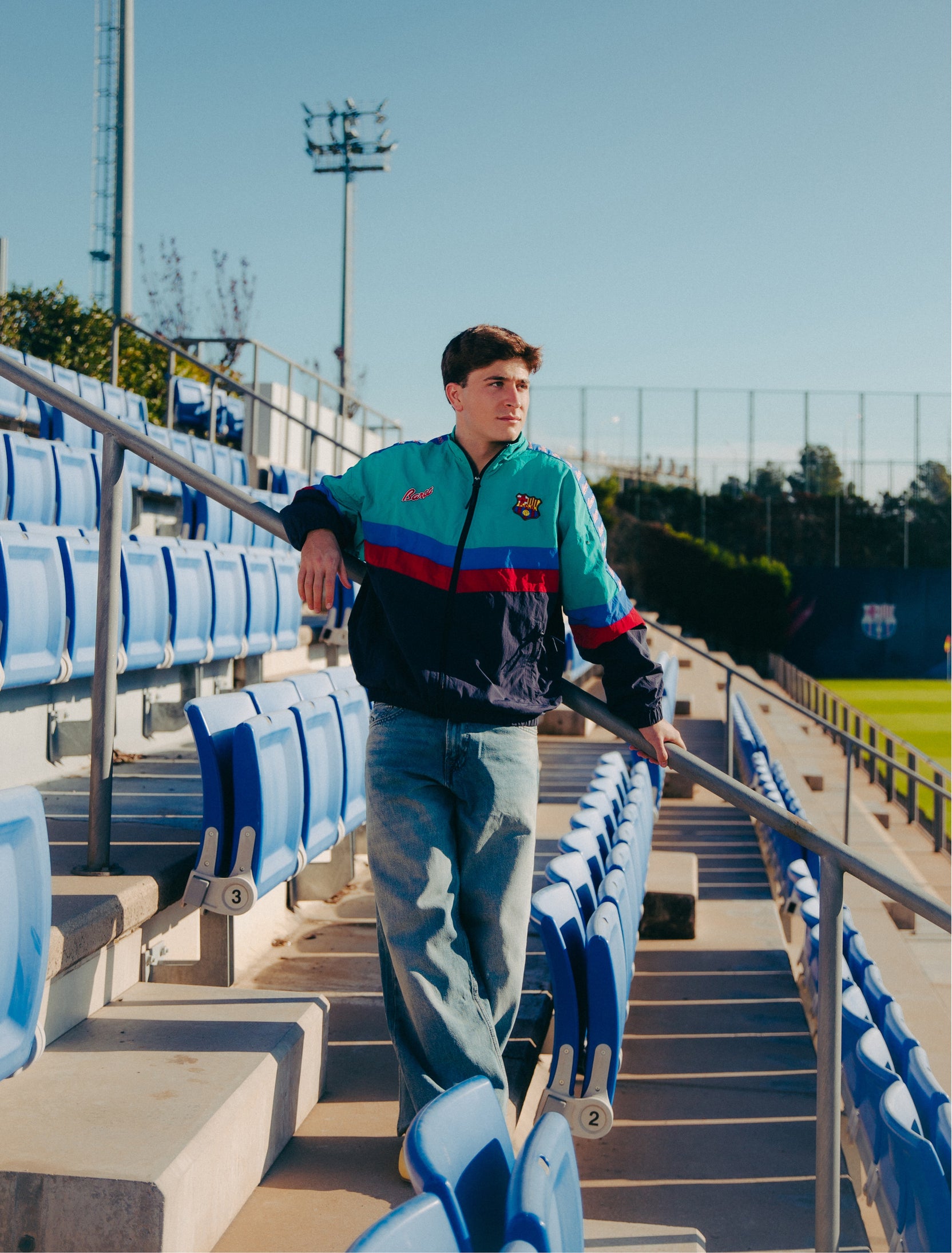 Retro-style windbreaker in teal, red, blue, and navy with FC Barcelona crest and embroidered 'Barça' text on the chest.