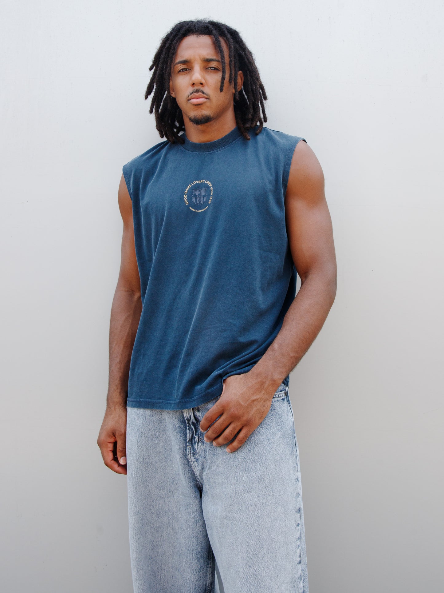 Jules Kounde wearing a sleeveless dark blue FC Barcelona T-shirt with circular crest print on the chest, paired with light denim jeans